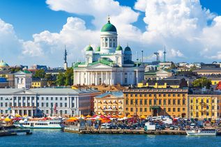 Blick auf Helsinki in Finnland mit vielen Gebäuden in heller Farbe und Blick auf eine große Kirche vom Hafen aus