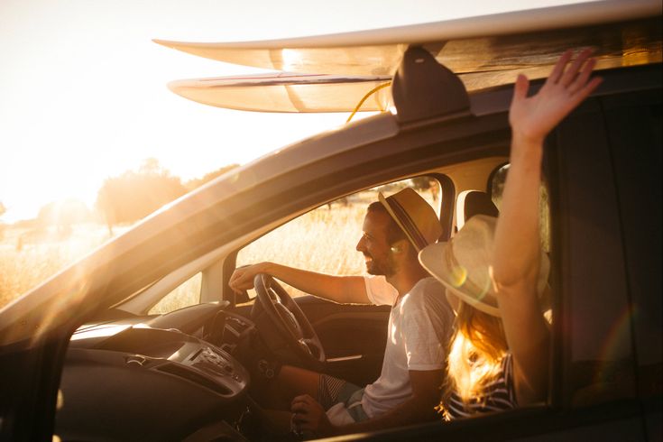 Eine Person fährt Auto, mit Surfbrettern auf dem Dach, bei Sonnenuntergang.