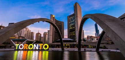 Blick auf die New City Hall, das neue Rathaus, mit seinen zwei geschwungenen Türmen. Im Vordergrund der beleuchtete, ikonische TORONTO Schriftzug bei Sonnenaufgang.