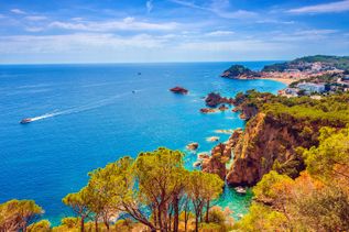 Luftaufnahme der Küste der Costa Brava, Spanien, mit türkisblauem Meer, Felsen und einer Stadt.