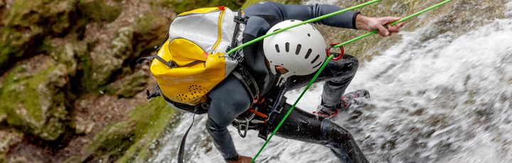 Ein Mann klettert an einer Felswand, während Wasser unter ihm lang fließt.