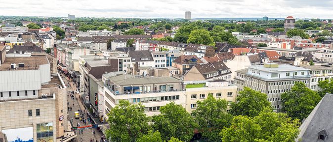 Stadtansicht von Essen mit Einkaufsstraße, modernen Gebäuden und grünen Baumkronen in einer lebendigen Innenstadt.