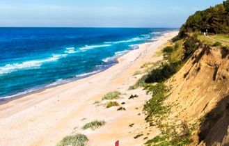 Luftaufnahme der polnischen Ostseeküste mit breitem Sandstrand, Meer und bewaldeter Steilküste unter blauem Himmel.