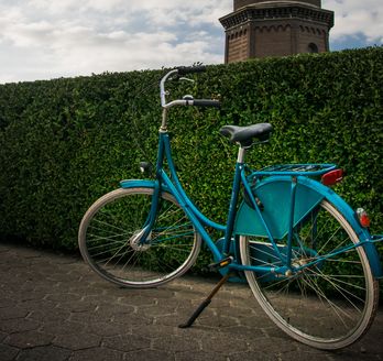 Blaues Fahrrad vor einer Hecke und dahinter ein Leuchtturm. 