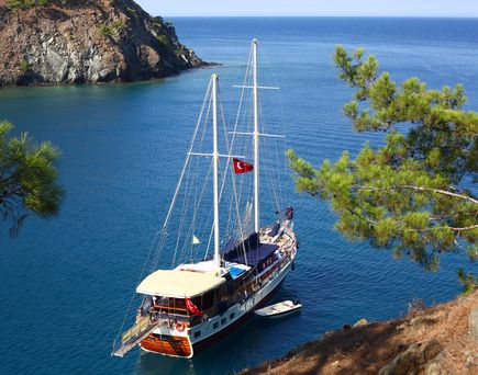 Blick eine Bucht mit Segelschiff, umgeben von Felsen und strahlendem Himmel