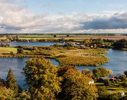 Landschaft mit Fluss, Seen und grüner Vegetation in ländlicher Umgebung unter leicht bewölktem Himmel.