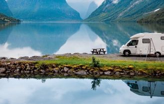 Weißer Campervan steht auf einer kleinen Landzunge im See, umgeben von Bergen und Wasser.
