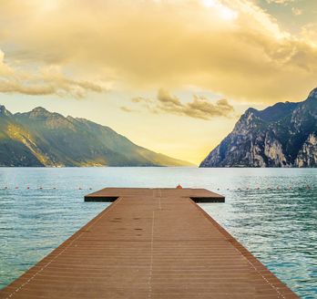Eine Holzbrücke, die in einen See oder Fluss führt, mit Bergen im Hintergrund.
