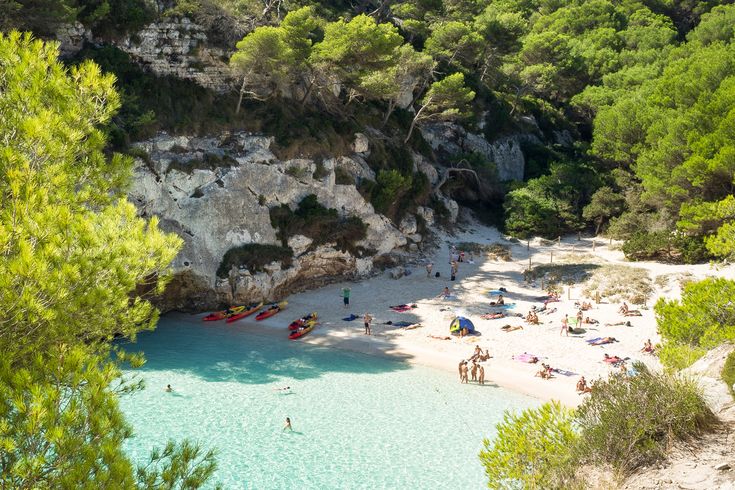 Eine Bucht mit Sandstrand und türkisblauem Wasser, umgeben von grüner Vegetation.