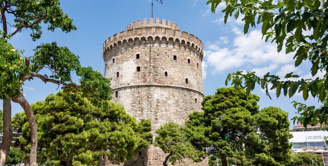 Ein historisches Gebäude mit einem Turm auf einem Hügel, umgeben von grünen Bäumen.