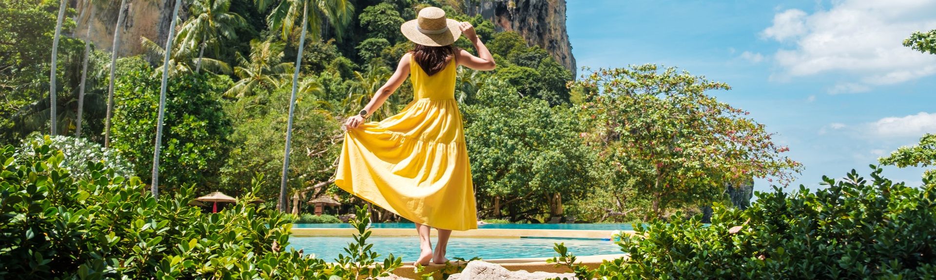 Frau in gelbem Kleid in einer natürlichen Landschaft mit Palmen und Felsen