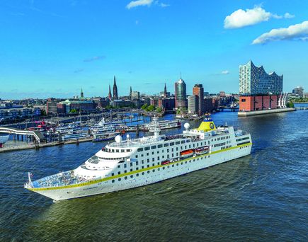 Kreuzfahrtschiff fährt durch das Meer mit Stadt im Hintergrund