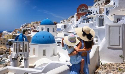 Eine Mutter und ihre Tochter stehen auf einem Balkon und blicken auf eine weiße Stadt und das Meer.