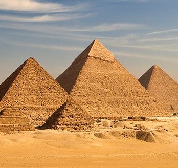 Weitläufiges Wüstenpanorama mit den eindrucksvollen Pyramiden von Gizeh vor der nahen Skyline Kairos.