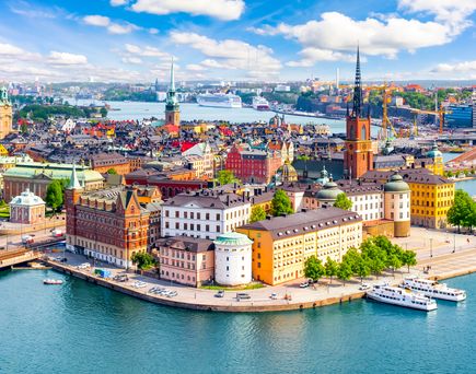 Eine beeindruckende Panoramaansicht von Stockholm, Schweden, mit ihren historischen Gebäuden, die sich entlang des Wassers erstrecken, und Booten, die im Hafen liegen, unter einem klaren blauen Himmel.