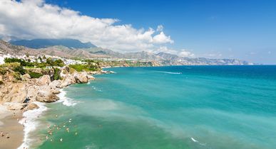 Ein Sandstrand mit klarem türkisfarbenem Wasser und grüner Vegetation.