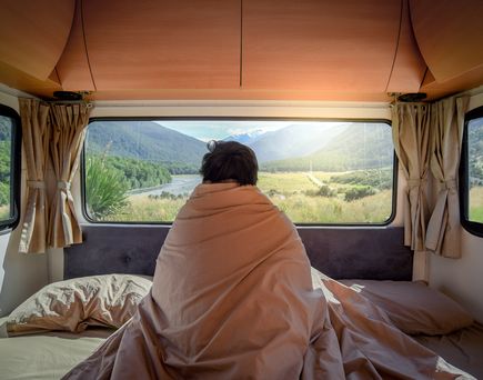 Ein Mann sitzt im geöffneten Wohnmobil und blickt in die weite Natur, warmes Licht.