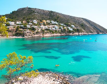 Blick auf die Bucht an der Costa Blanca. Türkises Meer und im Hintergrund Küste mit Häusern