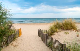 Ein Holzpfad führt über Sanddünen zum Strand in Languedoc-Roussillon, Frankreich, mit Meer und blauem Himmel.