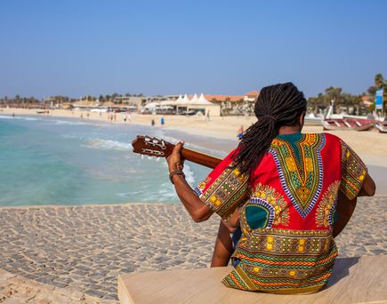 Musiker mit Gitarre und Rasta Haaren sitzt am Santa Maria Beach, Sal