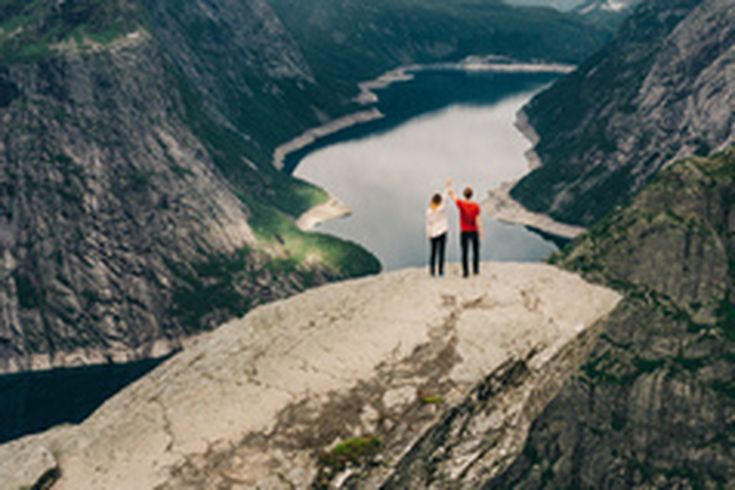 Eine Person steht auf der Trolltunga-Felsformation und blickt auf eine weite Landschaft.