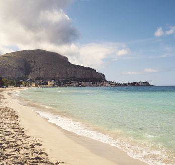 Ein Sandstrand mit türkisfarbenem Wasser, umgeben von Bergen.