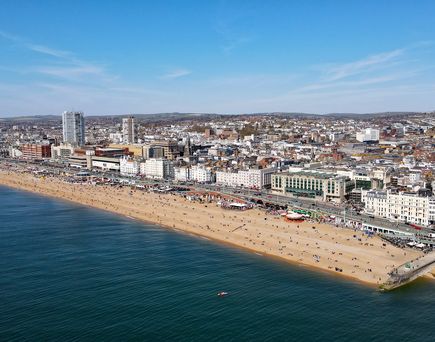 Blick aus Vogelperspektive auf das blaue Meer, den Strandabschnitt sowie die vielen Hotels im Hintergrund. Blauer Himmel