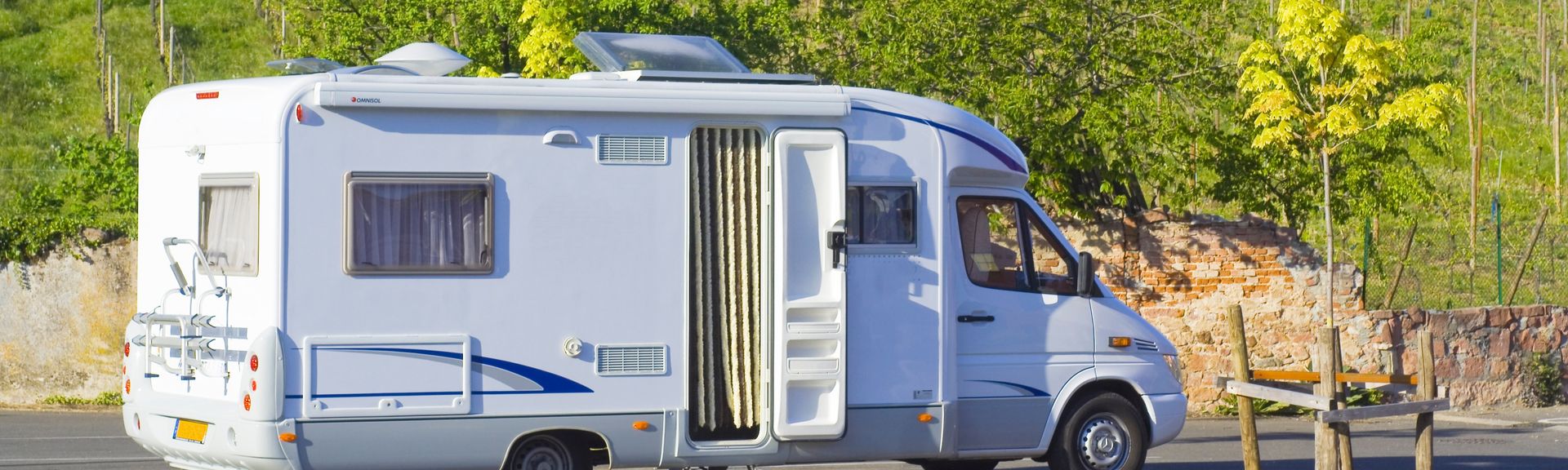 Weißer Campervan parkt am Straßenrand vor einem Wohnhaus in einer grünen Vorstadt.