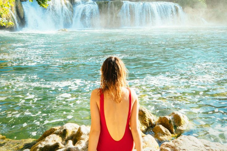 Eine Person sitzt an einem Wasserfall und blickt auf das Wasser.
