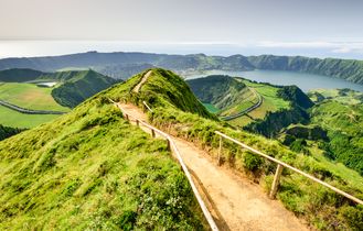 Eine grüne, hügelige Landschaft mit einem Pfad, der sich durch die Hügel schlängelt.