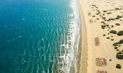Ein Sandstrand mit türkisfarbenem Wasser, umgeben von Gebäuden.