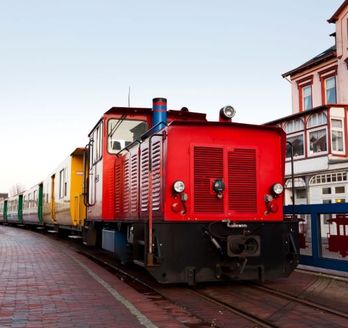 Kleinbahn Borkum. Roter Zug fährt durch die Stadt.