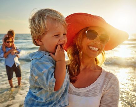 Eine Frau hält ein Kind im Arm am Strand.
