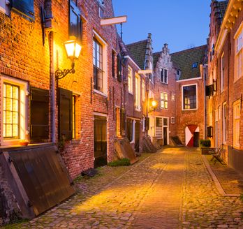Eine enge Gasse in einer Stadt bei Nacht, mit beleuchteten Gebäuden.