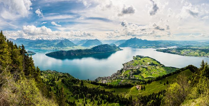 Vierwaldstättersee. Im Vordergrund grüne Landschaften, im Hintergrund der See. Blauer Himmel.