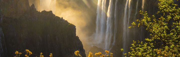  Die mächtigen Victoriafälle in Afrika, die riesige Wassermassen über eine breite Klippe in eine darunterliegende Schlucht stürzen lassen.