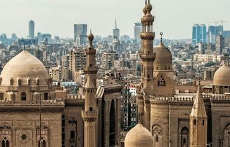 Eine Panoramansicht der Zitadelle von Kairo, mit mehreren großen Moscheen und Minaretten, die sich vor der modernen Skyline der Stadt abzeichnen.