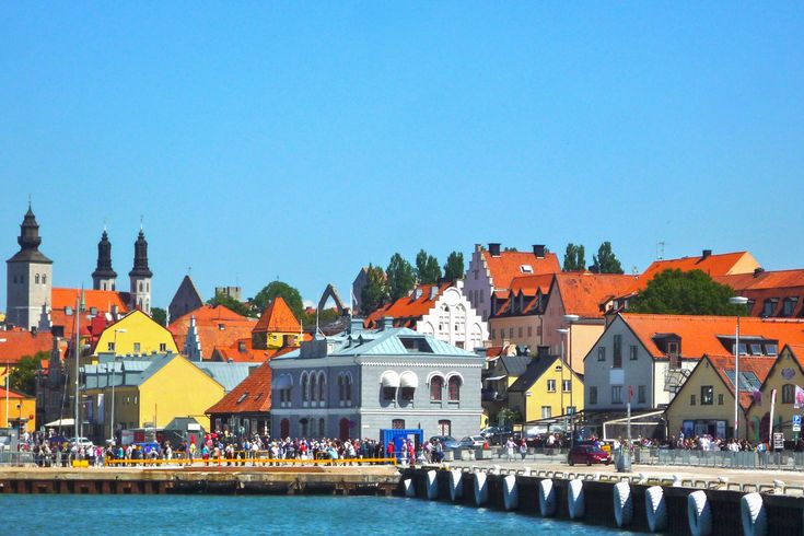Blick auf die bunten Häuser von Visby, ein Steg am Wasser, Cafe und Sitzmöglichkeiten dort. Blauer Himmel.