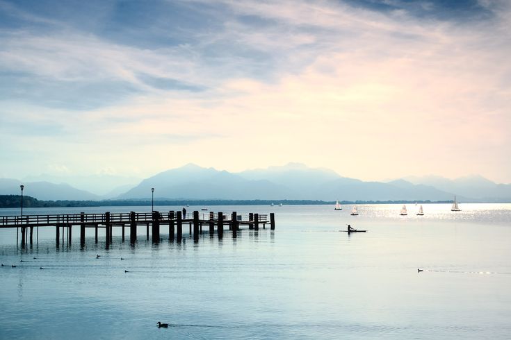 Ein langer Holzsteg führt in einen ruhigen See, umgeben von grüner Landschaft bei Sonnenuntergang.