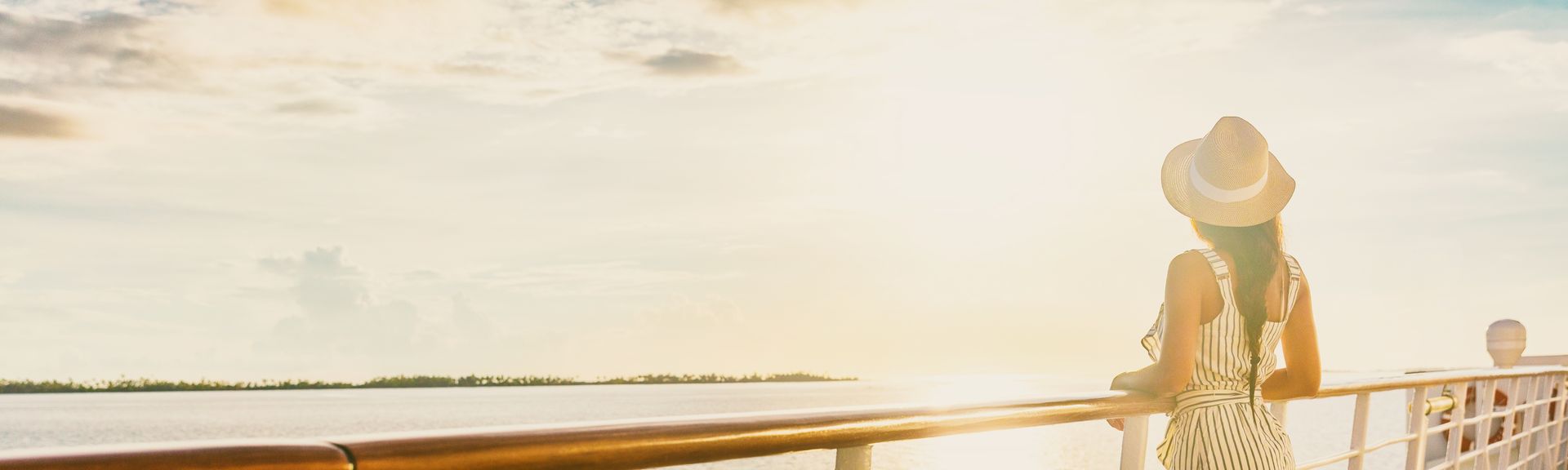 Frau mit Hut blickt auf einem Kreuzfahrtschiff in den Sonnenuntergang