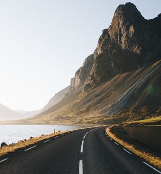 Küstenstraße in Island entlang einem Gewässer in Richtung felsigem Berg