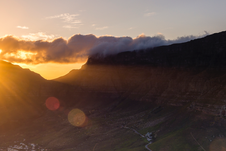 Eine spektakuläre Luftaufnahme des Tafelbergs in Kapstadt, Südafrika, bei Sonnenuntergang, mit der Stadt, die sich am Fuße des Berges ausbreitet und die Bucht überblickt.