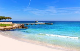 Ein Sandstrand mit türkisblauem Wasser und einem bewölkten Himmel.
