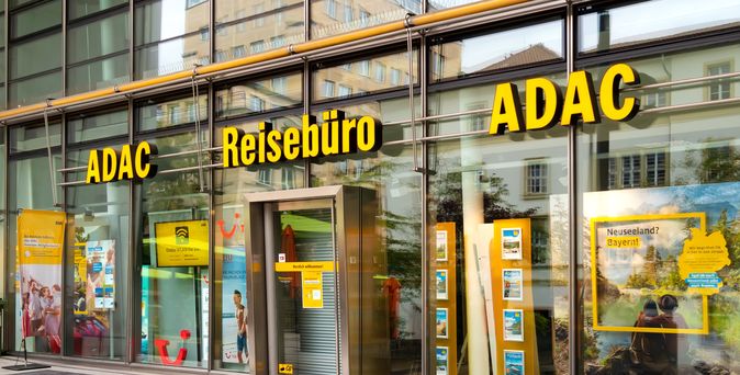 ADAC Reisebüro mit großer Glasfassade, gelbem Logo und Schaufenstern voller Reiseplakate in einer Innenstadtlage.