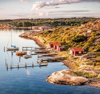 Eine malerische Küstenlandschaft mit bunten Häusern, die sich an einen Hang schmiegen, und Booten im ruhigen Wasser. Die Szene ist lebhaft und einladend.