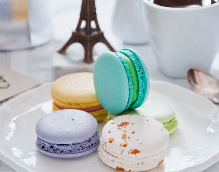 Eine Platte mit bunten Macarons und einer Tasse Kaffee. Die Macarons sind in Pastellfarben gehalten, und die Szene ist hell und appetitlich.