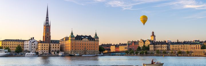 Blick auf die Silhouette von Riddarholmen gegen das Wasser, ein gelber Heißluftballon schwebt über den Gebäuden, Boot fährt vorbei, Stockholm, Schweden