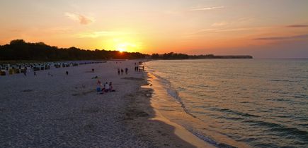 Sonnenuntergang am Sandstrand von Usedom mit Spaziergängern am Wasser.