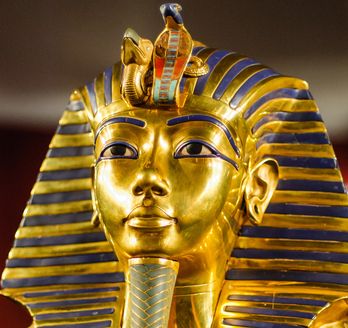 Eine Nahaufnahme zeigt die goldene, mit blauen Lapislazuli-Streifen verzierte Totenmaske des Pharaos Tutanchamun.