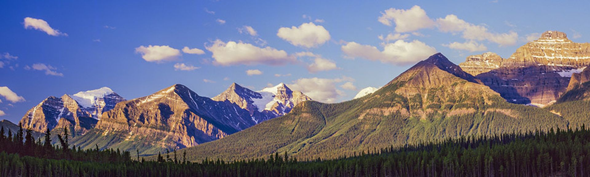 Eine beeindruckende Panoramaansicht des Banff Nationalparks in den Rocky Mountains, Alberta, Kanada, mit schneebedeckten Gipfeln und einem klaren, blauen See im Vordergrund.